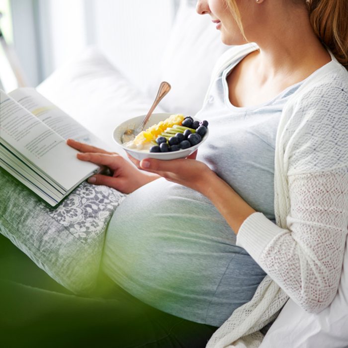 Young mother eating and reading book at home