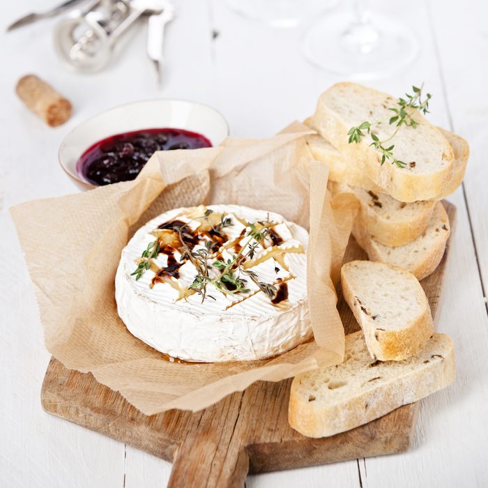 baked camembert cheese with thyme and toasted bread on wooden board