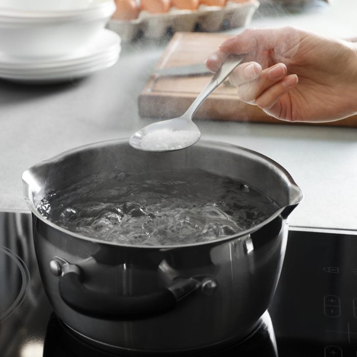 Woman salting boiling water in pot on stove, closeup; Shutterstock ID 1295704264