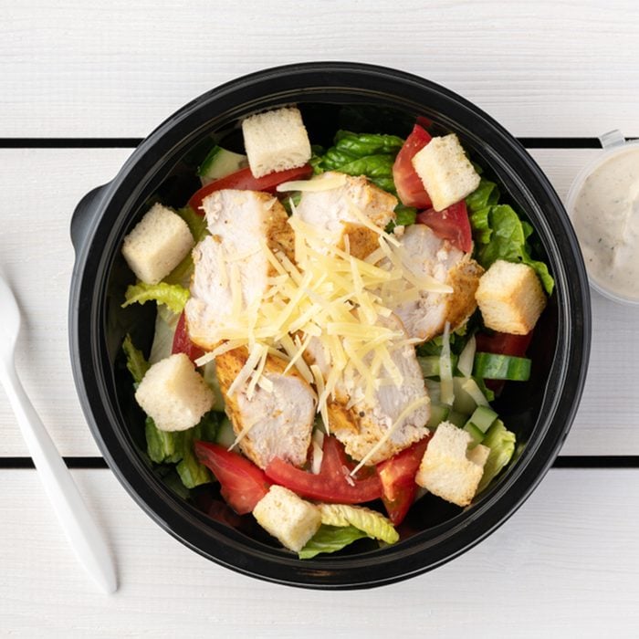 Caesar salad in round black lunchbox on wooden bacground; Shutterstock ID 1315532318; Job (TFH, TOH, RD, BNB, CWM, CM): TOH