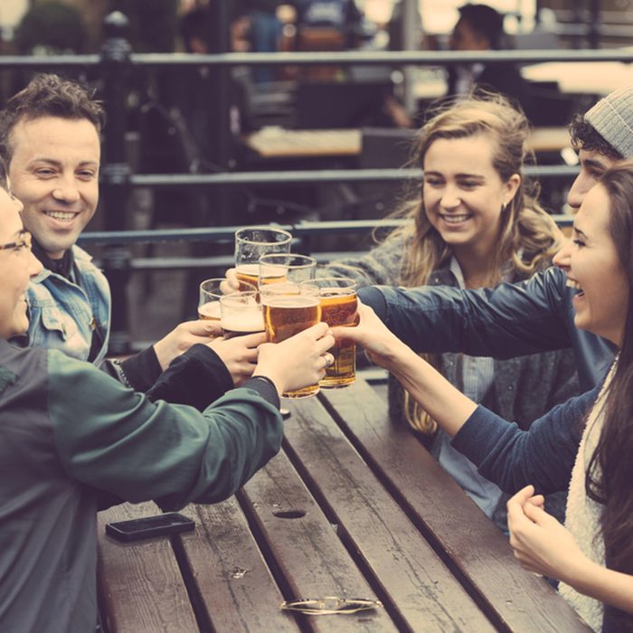 Group of friends enjoying a beer at pub in London, toasting and laughing.