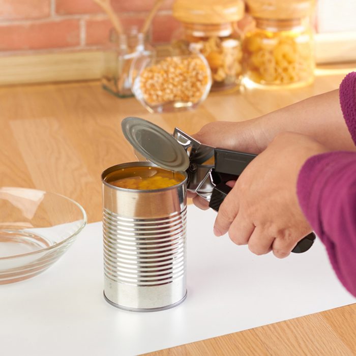 Woman opening a can of corn with can opener in the kitchen