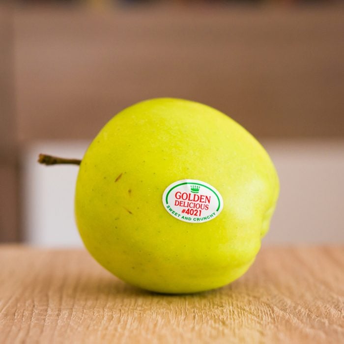 Fresh green golden delicious apple with brand sticker on a wooden table in soft focus on August 2017 in Poznan, Poland