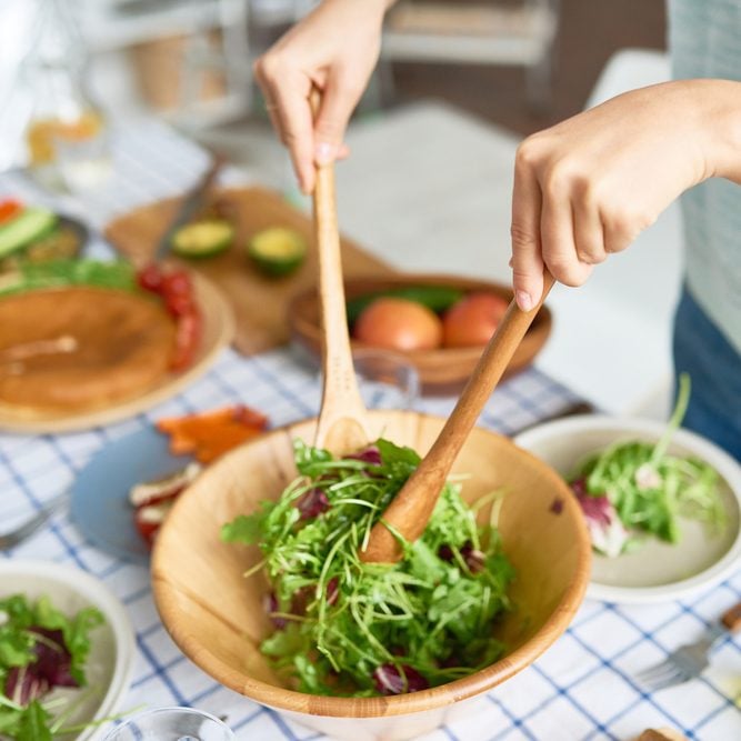 Closeup of young woman mixing green salad in wooden bowl at table with wholesome food while preparing family dinner; Shutterstock ID 734792491; Job (TFH, TOH, RD, BNB, CWM, CM): TOH Superfoods