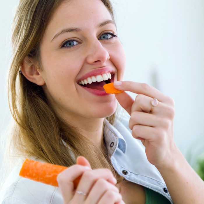 Portrait of pretty young woman eating carrot in the kitchen.