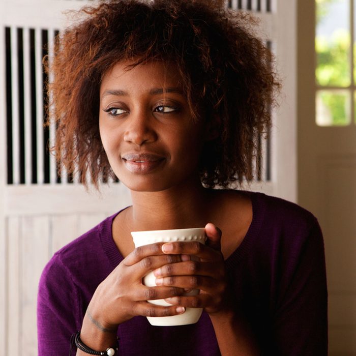 Close up portrait of a beautiful young african american woman enjoying cup of coffee at home