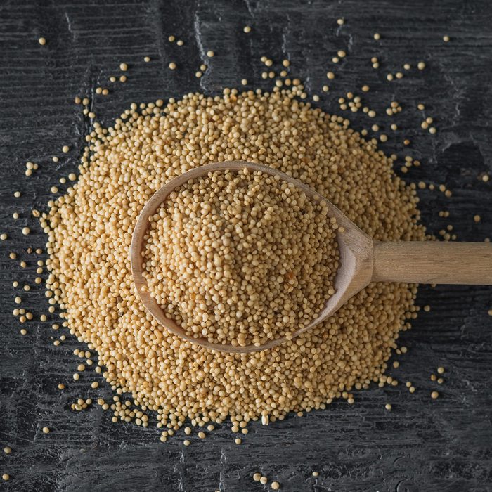 A pile of amaranth seeds and a wooden spoon on a dark wooden table. 