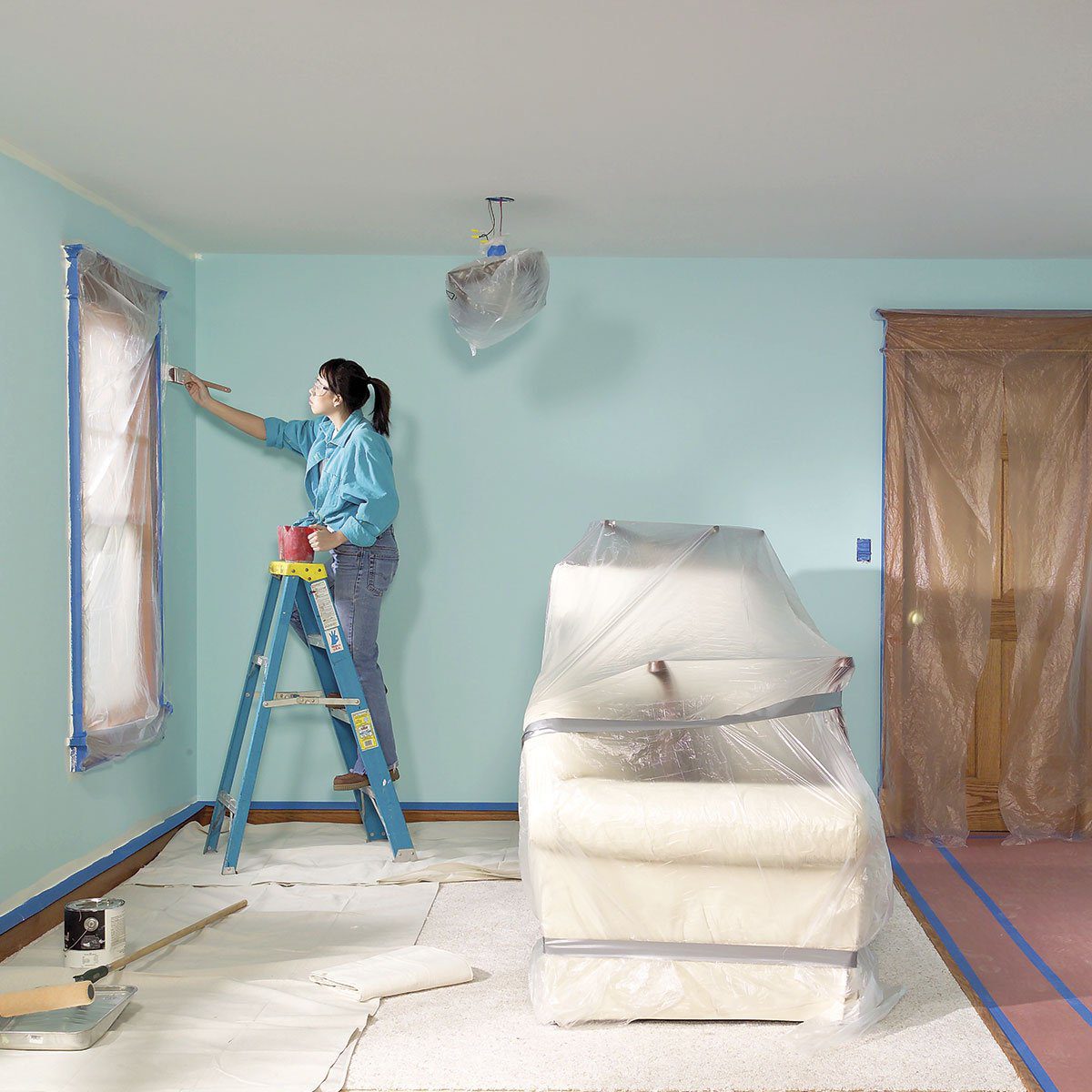 Woman on a ladder painting a room blue