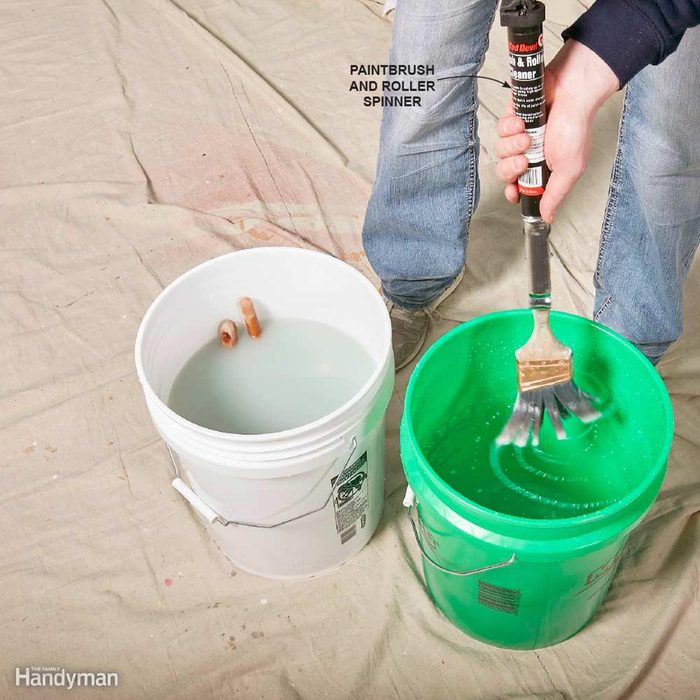 Cleaning a brush in a large green bucket of water