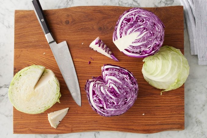 Knife And Cabbage On Cutting Board. cabbage heads have been sliced in half with stalks cut out