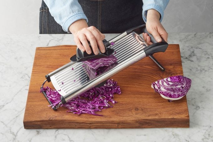Cabbage Being Sliced with a mandoline over a wood cutting board