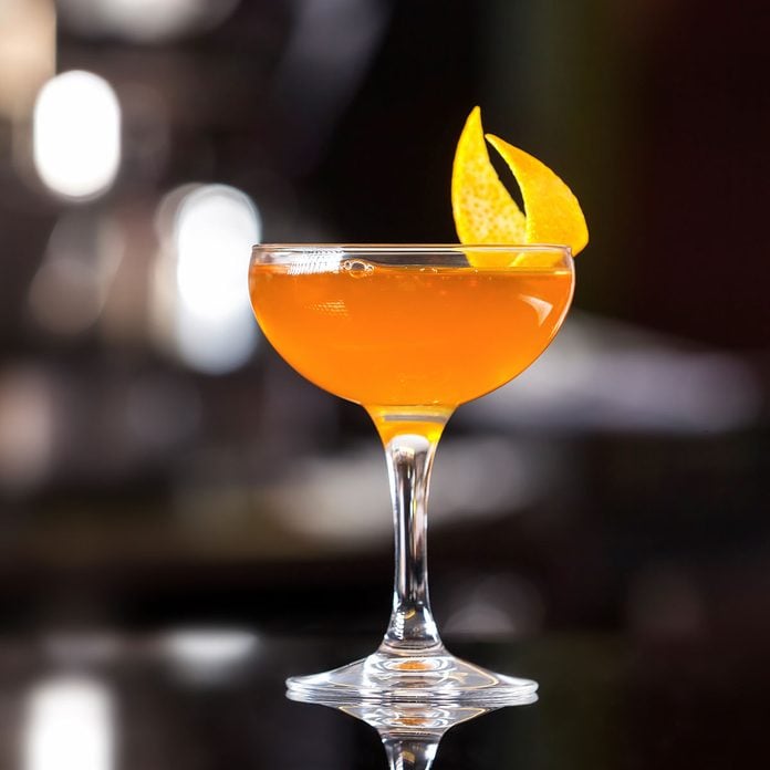 Glass of sidecar orange cocktail decorated with lemon at bar counter background.