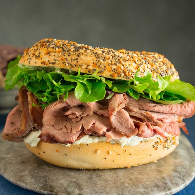 Roast beef sandwich with lettuce on an everything bagel with a side of blue corn chips