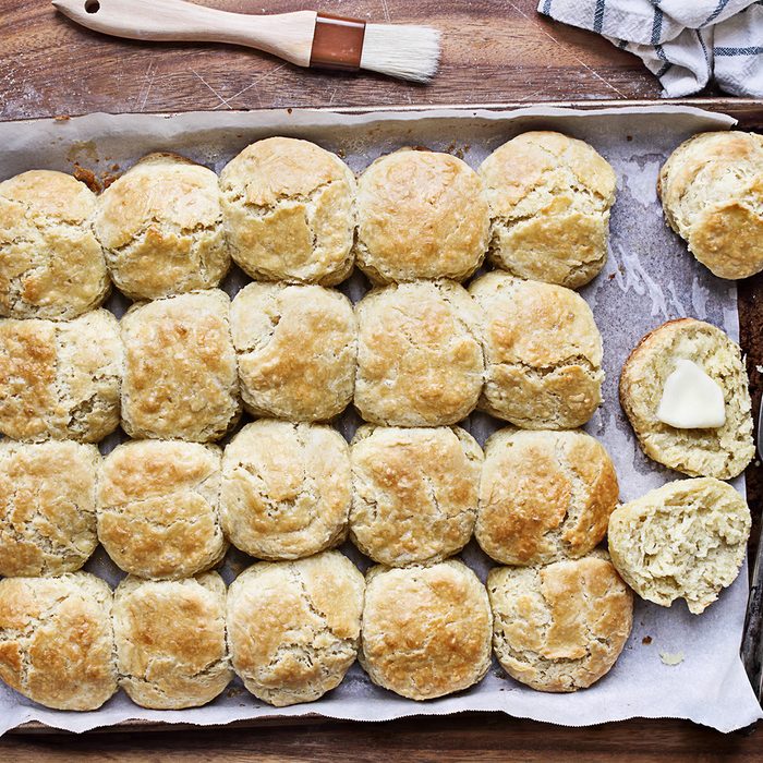 Freshly baked buttermilk southern biscuits or scones from scratch with rolling pin and basting brush on a baking sheet.