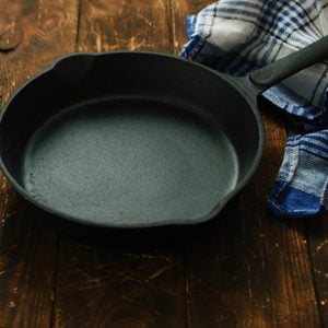 Simple black colored cast iron pan with checkered towel on wooden shabby table surface