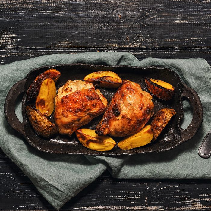 Chicken thigh baked with potatoes on a black dish.