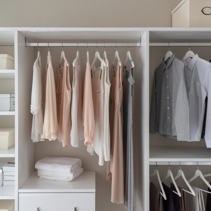 Modern closet with clothes hanging on rail, white wooden wardrobe