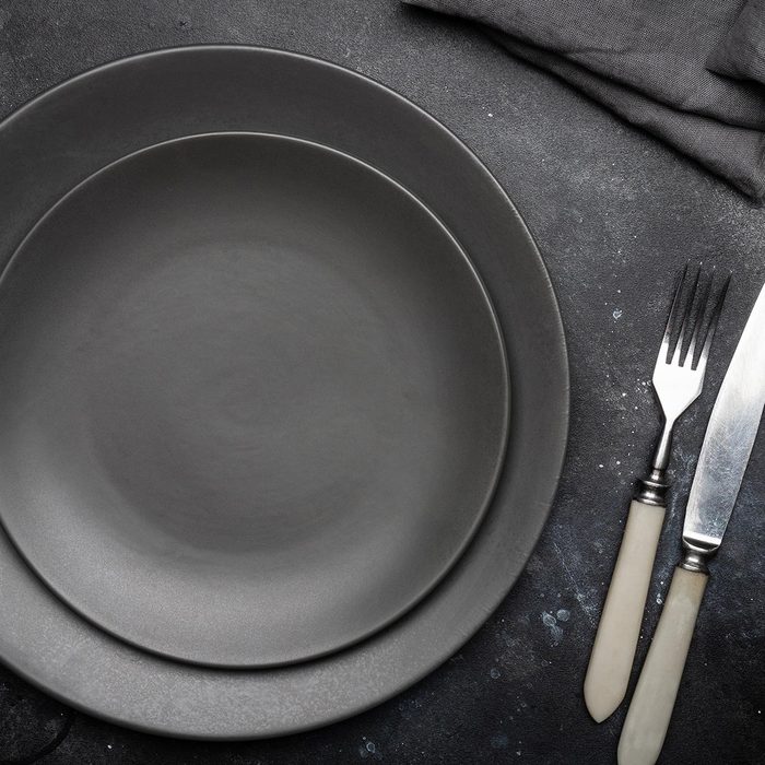 Empty gray plate (ceramic) on a dark gray background with a knife and fork, decorated with a bouquet of lavender and a napkin.