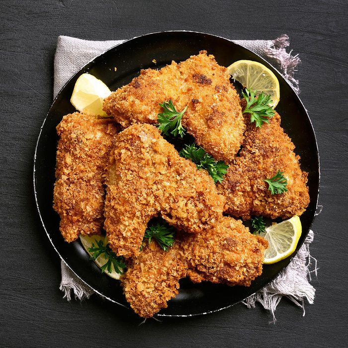 Fried breaded chicken wings on plate over black background.