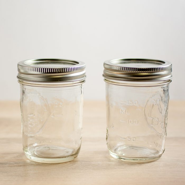 Empty canning jars await use on a wooden table.
