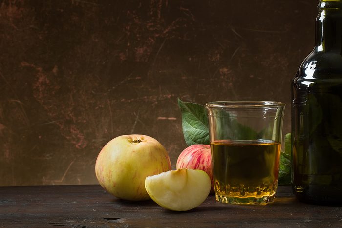 Glass of cider with apples and bottle on rustic wooden background