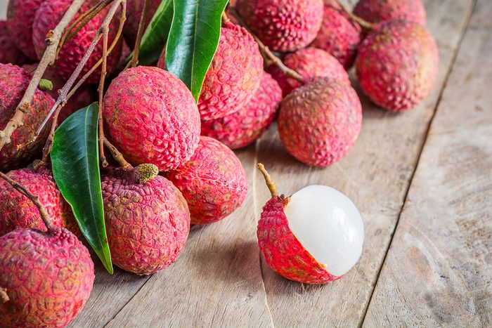 Lychee, Fresh lychee and peeled showing the red skin and white flesh with green leaf on a wooden background