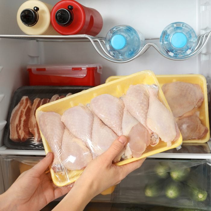 Woman taking raw chicken drumsticks from refrigerator, closeup