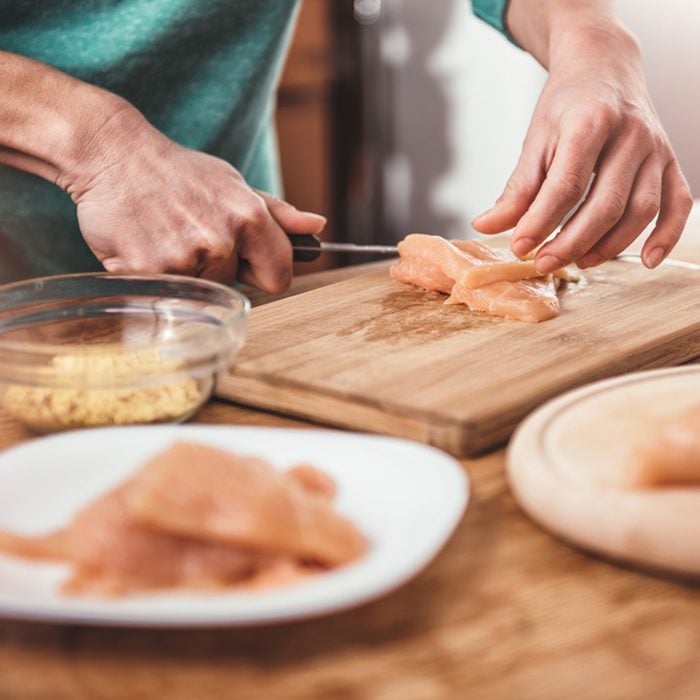 Woman cutting chicken breast on the table