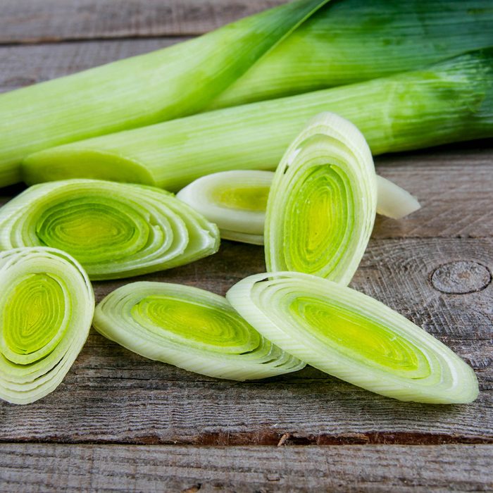 Fresh leeks whole and sliced on a wooden kitchen board; Shutterstock ID 583263889