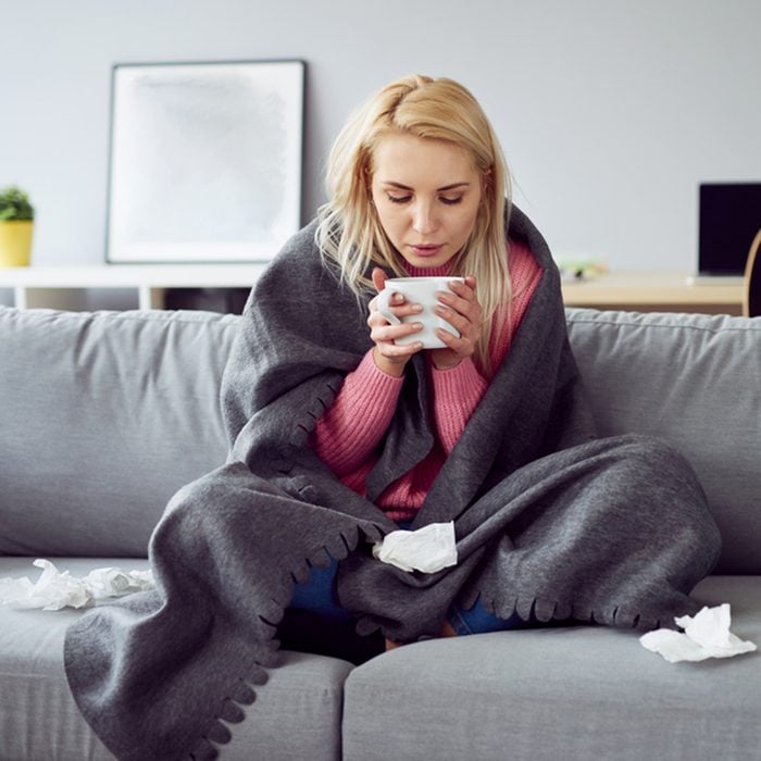 Young sick woman sitting on sofa drinking tea