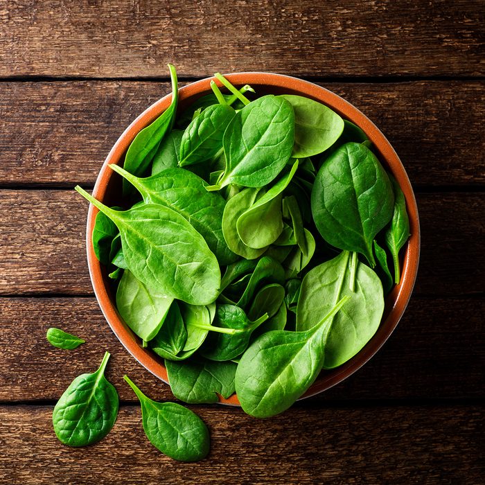Fresh spinach leaves in bowl on rustic wooden table.