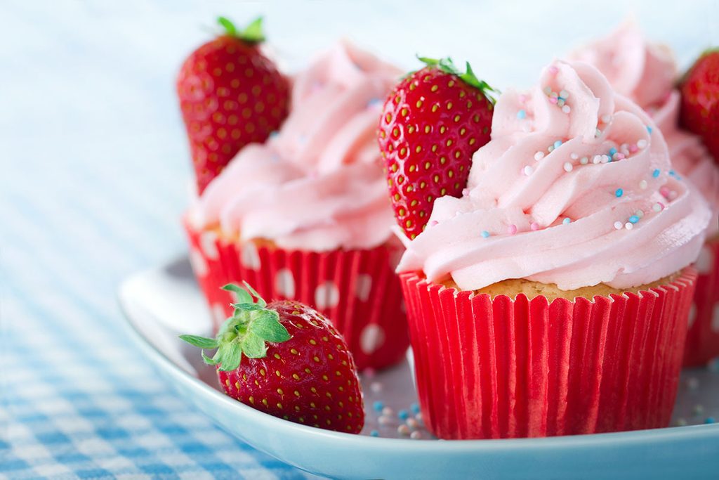 Pink cupcakes with fresh strawberries and sprinkles on a vintage tray and blue retro towel