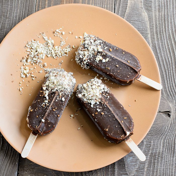 Chocolate popsicles with nuts on a brown wood background