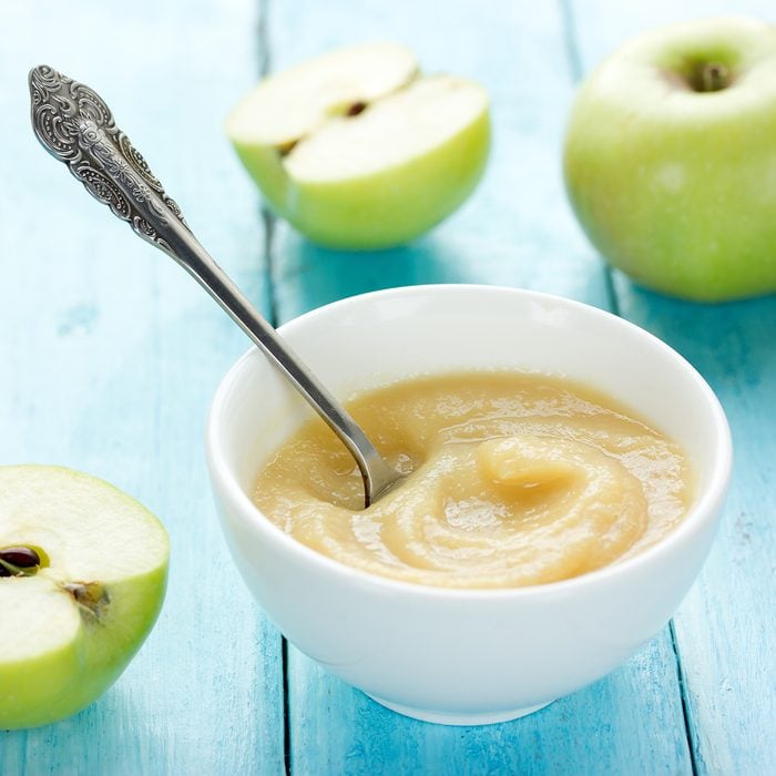 Healthy organic applesauce (apple puree, mousse, baby food, sauce) in white bowl on table with green apples