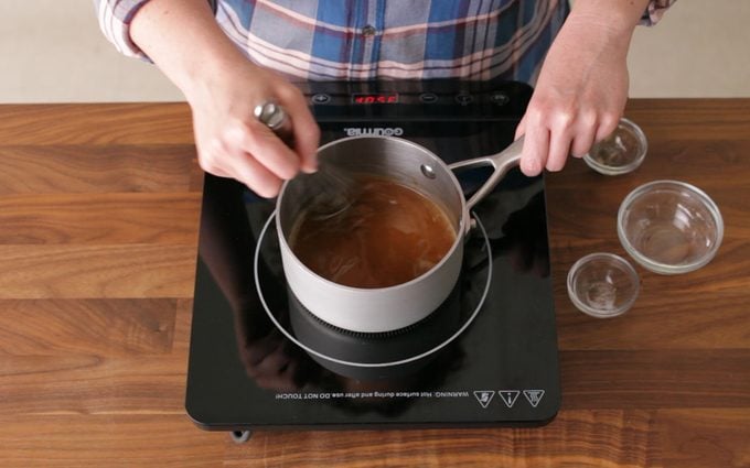 person stirring a Brown Roux in a sauce pan on a hot plate on a wood kitchen counter