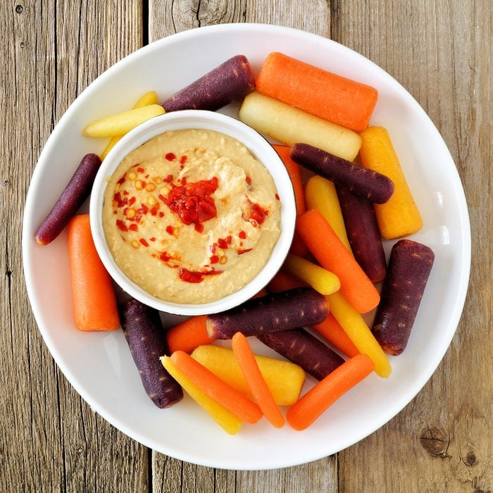 Plate of baby rainbow carrots with hummus dip, overhead view on a rustic wooden background