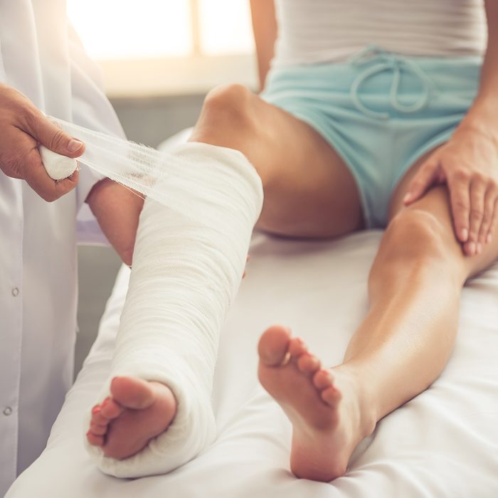 Cropped image of handsome doctor bandaging woman's broken leg while working in his office