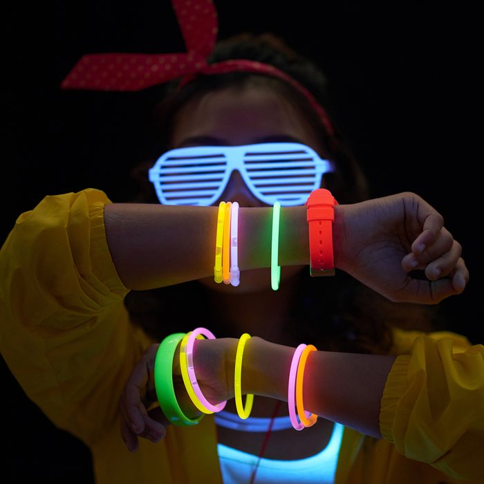 Cheerful young woman with neon bracelets in dark room