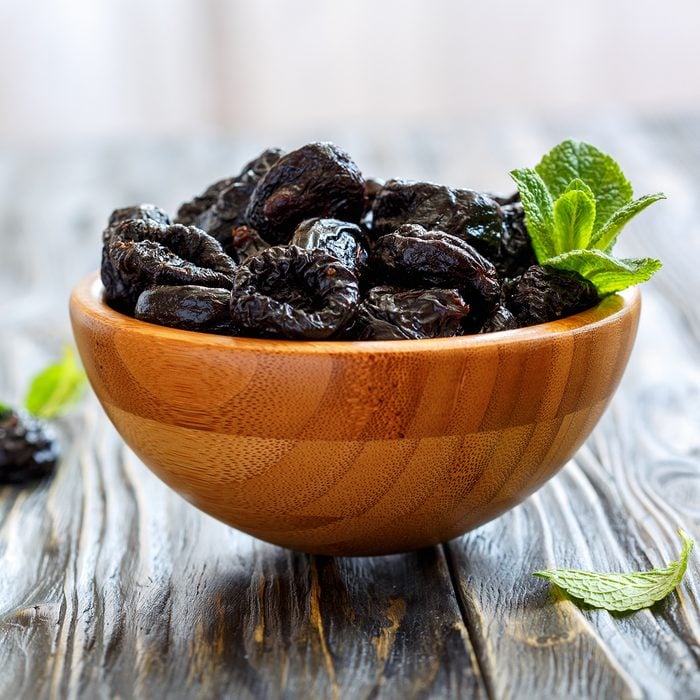 Prunes and mint in a bowl on old wooden table, selective focus.