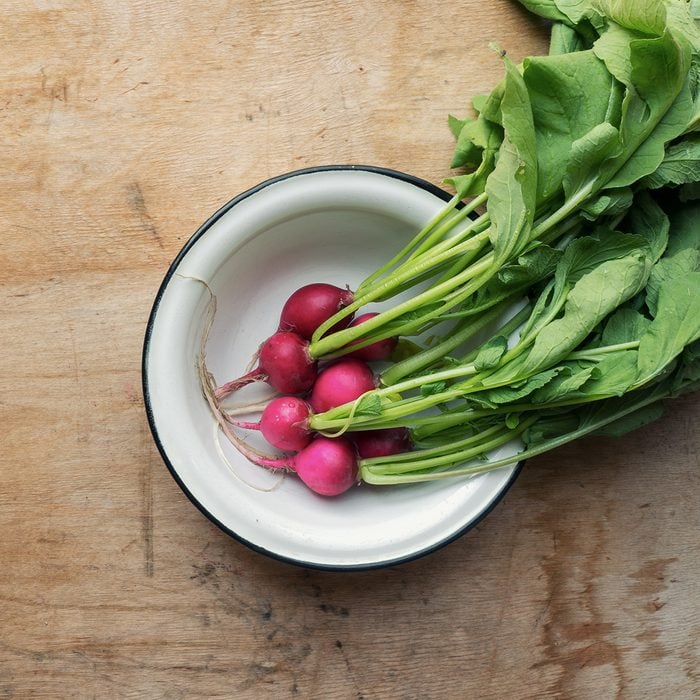 Fresh red radish in plate on wooden background.