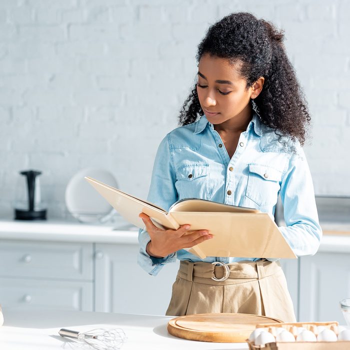 attractive african american woman reading cookbook in kitchen; Shutterstock ID 1229629288; Job (TFH, TOH, RD, BNB, CWM, CM): TOH