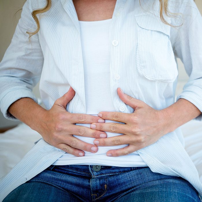woman sitting on her bed clutching her stomach in discomfort; Shutterstock ID 388594315; Job (TFH, TOH, RD, BNB, CWM, CM): Taste of Home