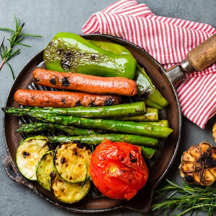Grilled sausages and green vegetables - zucchini, asparagus, bell pepper, garlic, lemon and rosemary on cast iron grill pan.