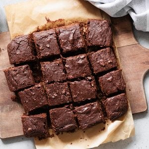 Chocolate brownie squares with walnuts on cutting board, top view