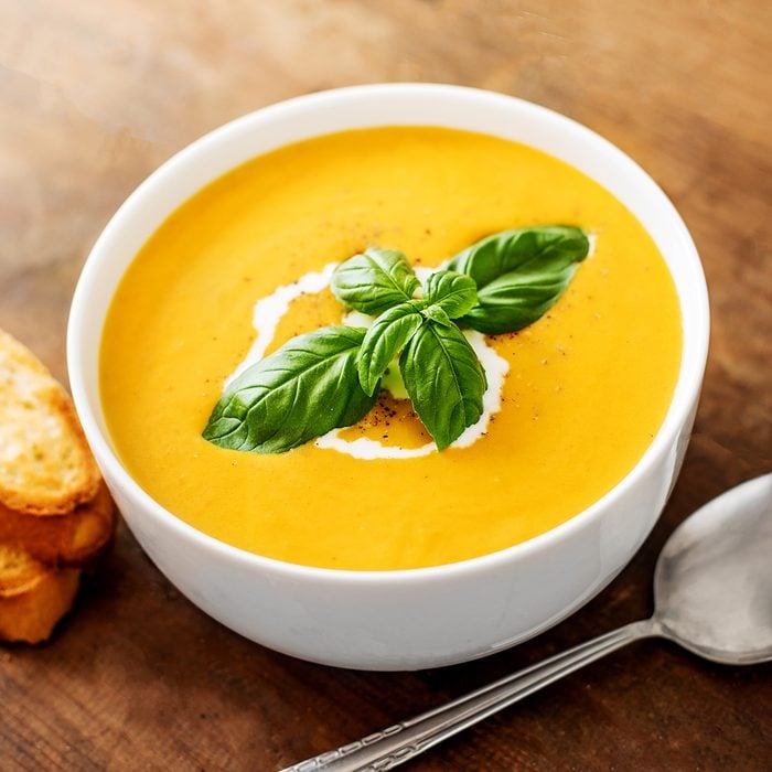 Bowl of squash soup with basil leaf on wood table.