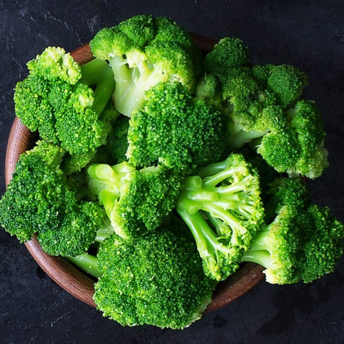 Fresh raw broccoli in a wooden bowl on a dark background