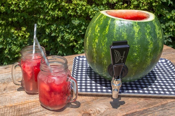 watermelon keg on an outdoor table with two mason jar mugs next to it