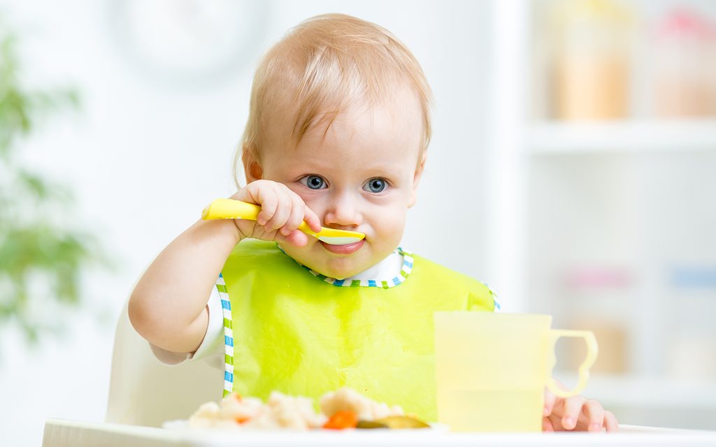 happy baby child sitting in chair with a spoon