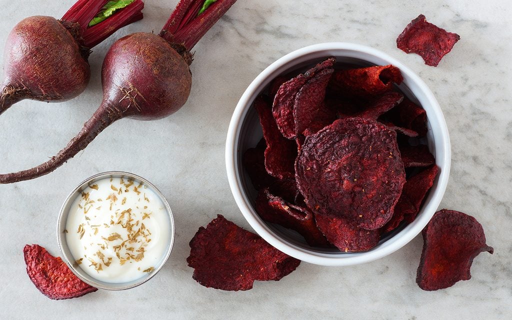 Bowl of healthy beet chips above view over a white marble background