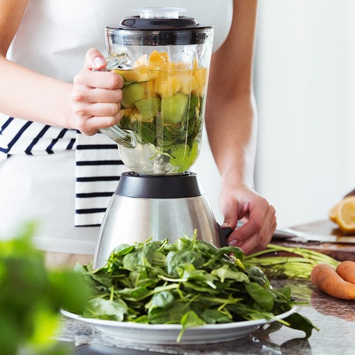 Vegetarian preparing vegan smoothie with rucola, citrus, cucumber in kitchen with carrots on countertop